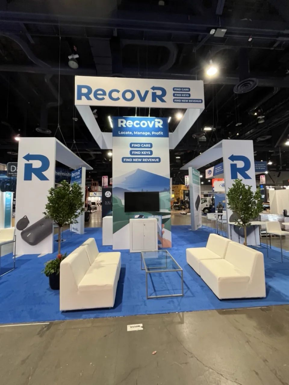 RecovR exhibit with blue carpet, white lounge seating and hanging sign